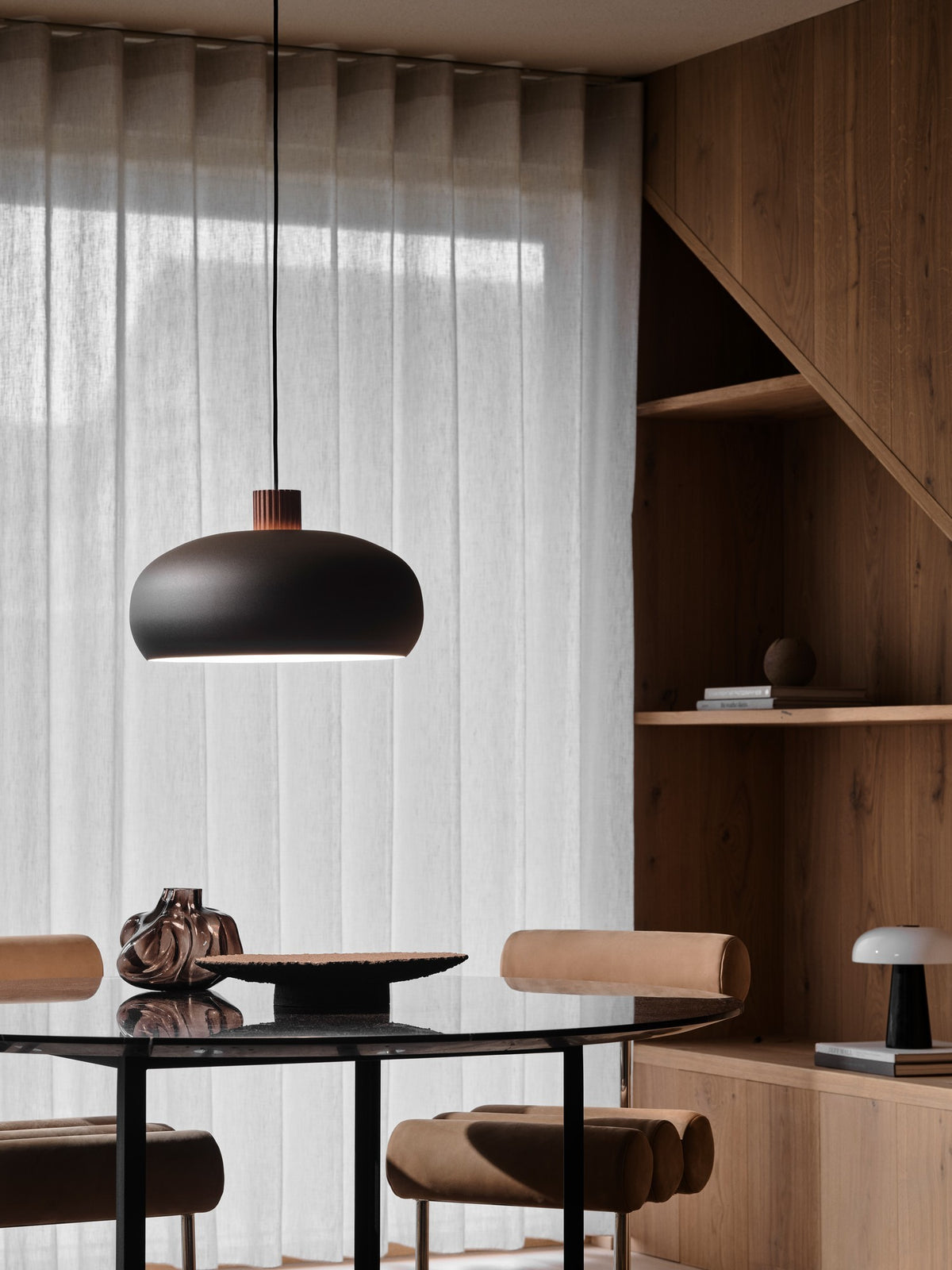 Mise en ambiance au-dessus d'une table à manger, suspension noire allumée dans un intérieur bois