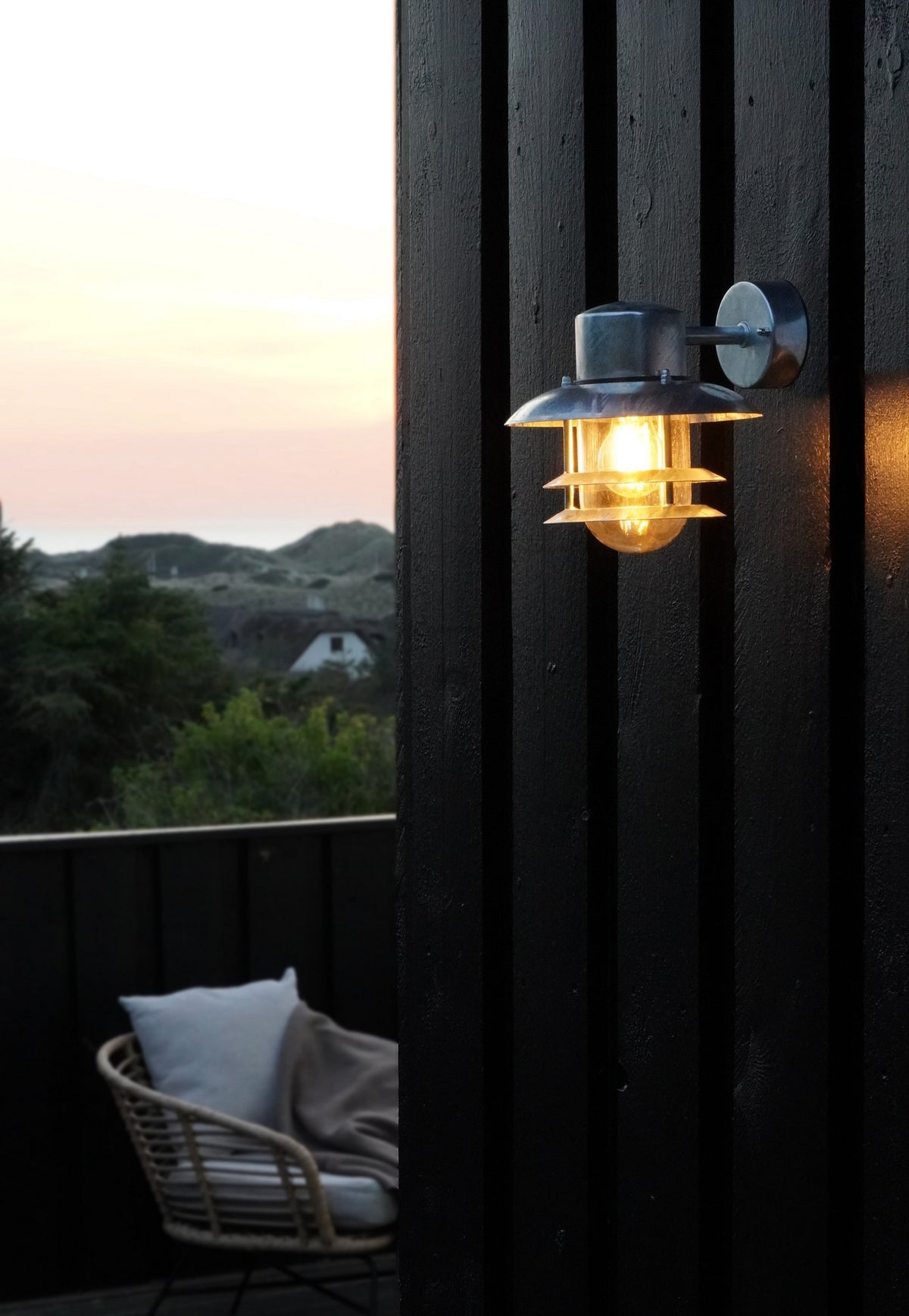 Mise en ambiance du luminaire allumé sur une façade en bois noir au crépuscule.