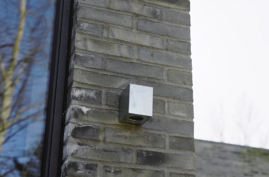 Applique extérieure grise fixée sur un mur de briques, vue rapprochée.