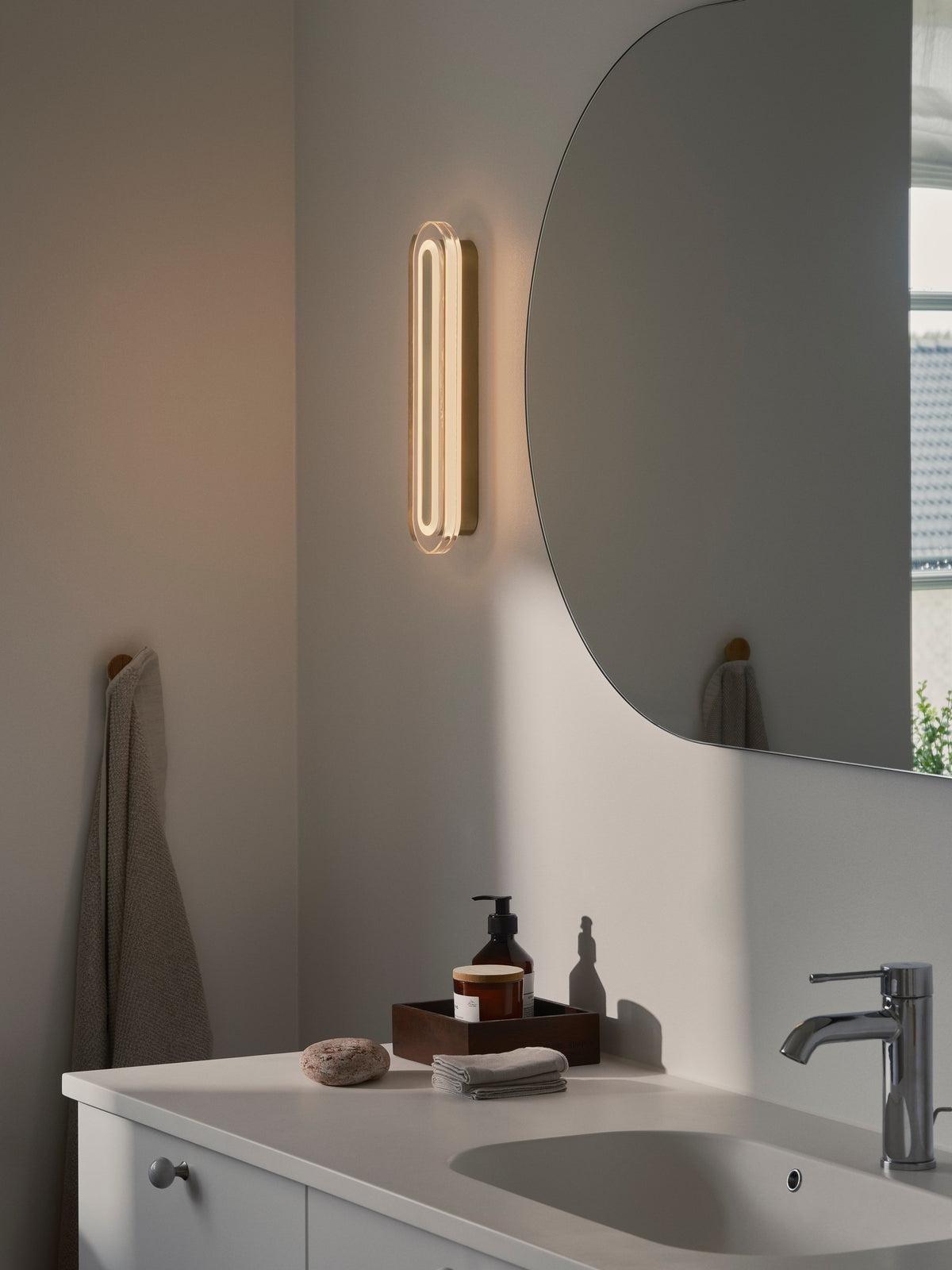 Ambiance de salle de bain avec applique murale allumée près d'un miroir et d'un lavabo.