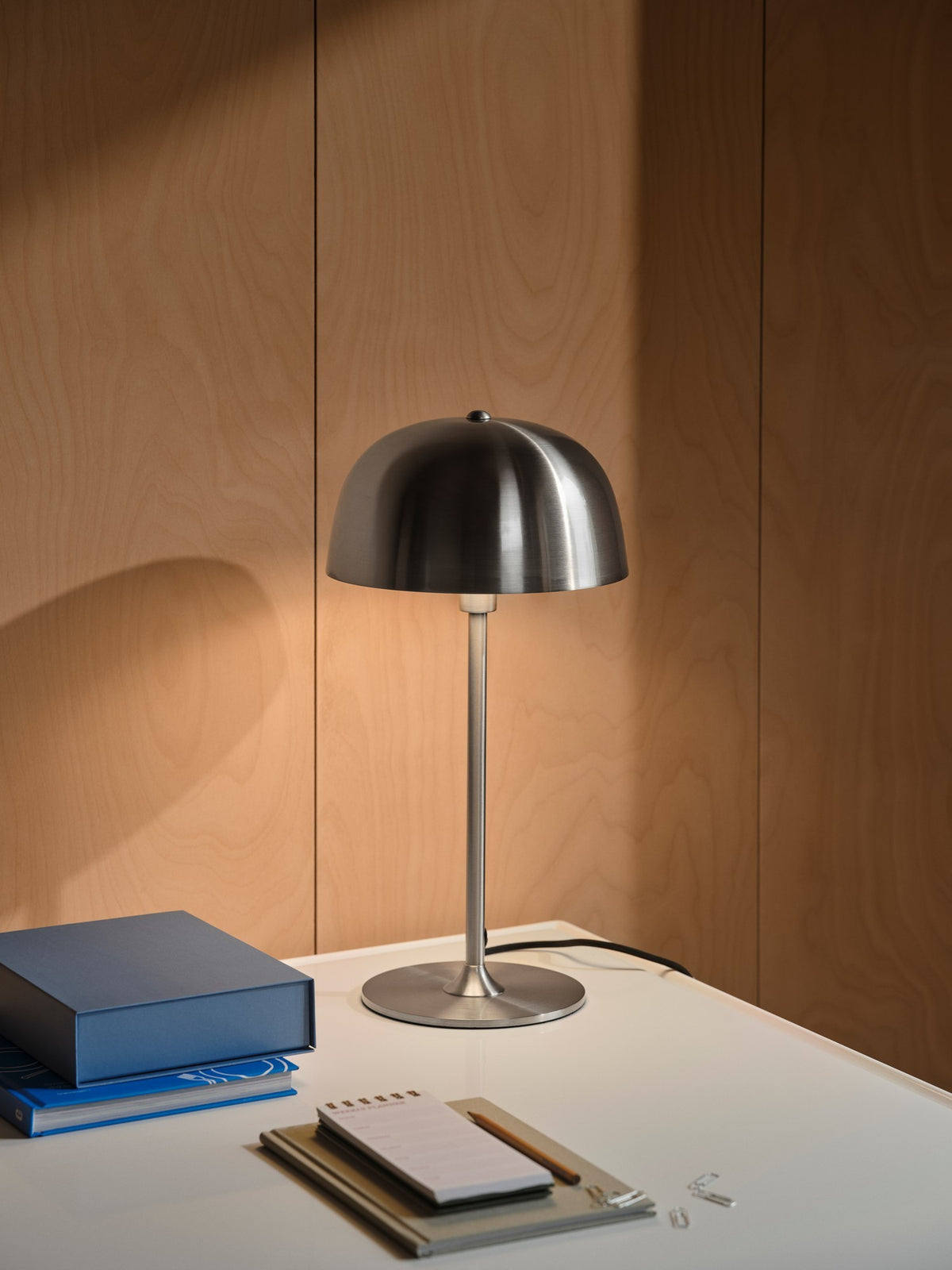 Mise en ambiance : lampe posée sur un bureau en bois avec carnets et livres