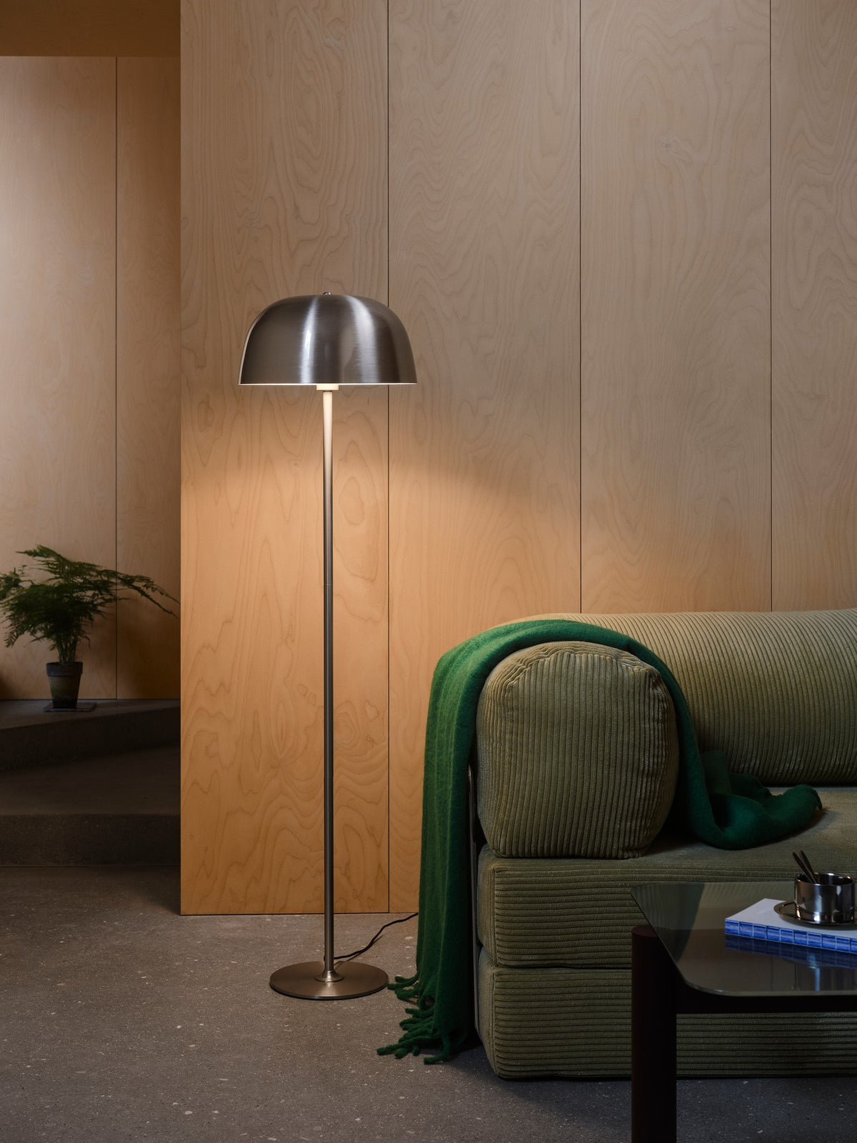Mise en ambiance du lampadaire allumé près d'un canapé vert devant une cloison bois