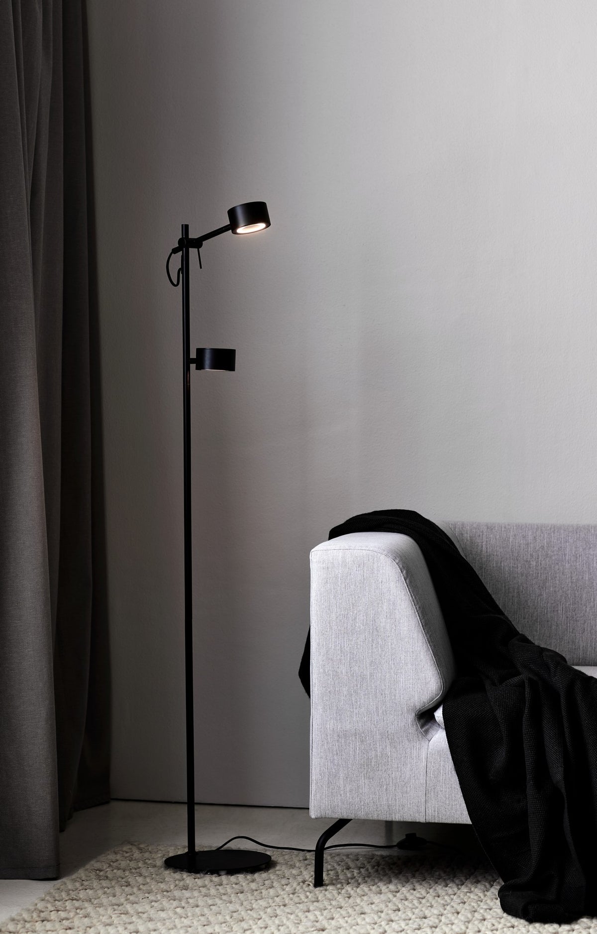 Mise en ambiance du lampadaire allumé près d'un canapé gris et d'un tapis.