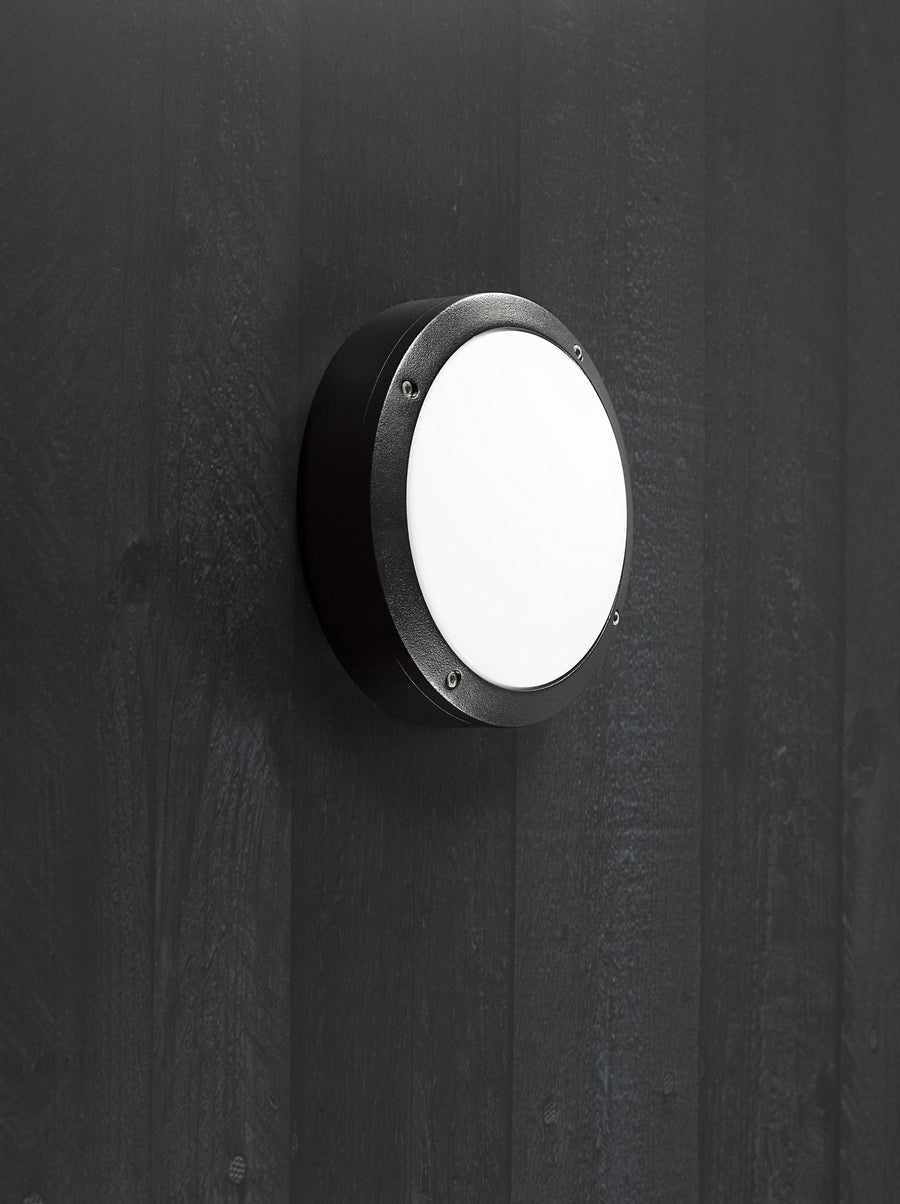 Luminaire extérieur noir installé sur une paroi sombre, lumière allumée