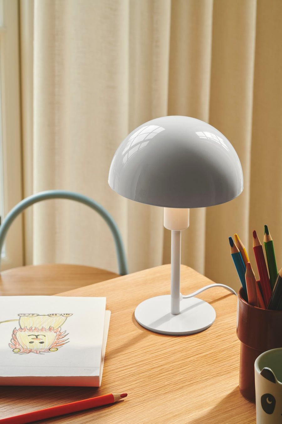 Lampe posée sur un bureau en bois près de crayons et d'un dessin