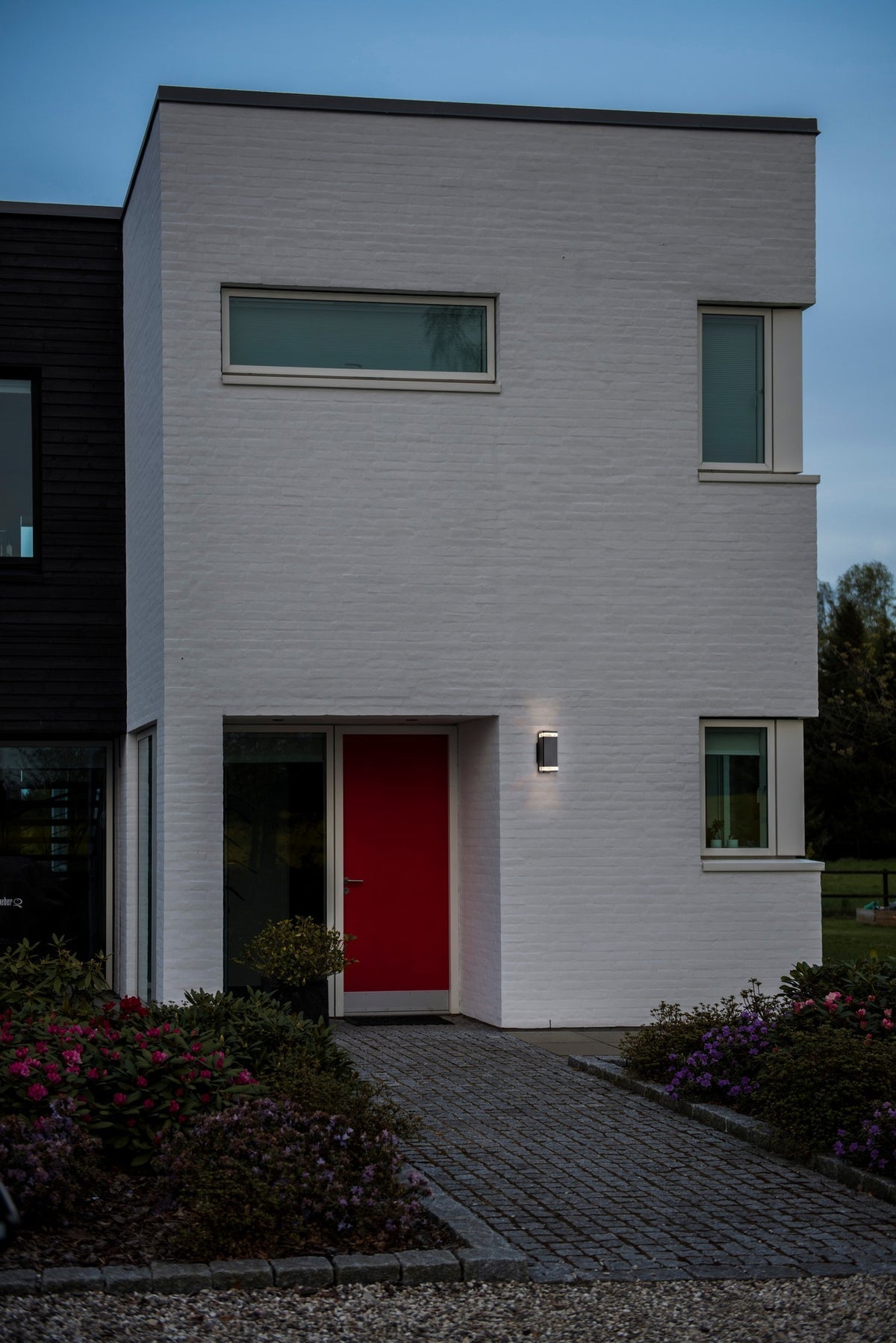 Applique allumée sur façade en brique blanche, à côté d'une porte rouge en soirée