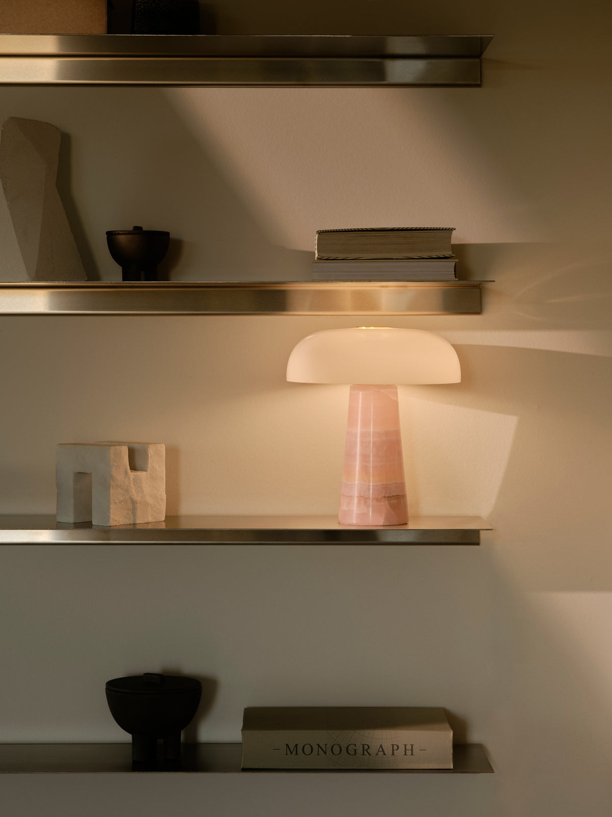 Lampe rose allumée posée sur une étagère, ambiance chaleureuse avec livres.