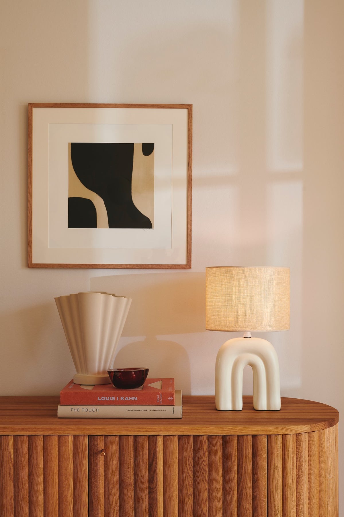 Mise en ambiance sur un meuble en bois, lampe beige près d'un vase et de livres