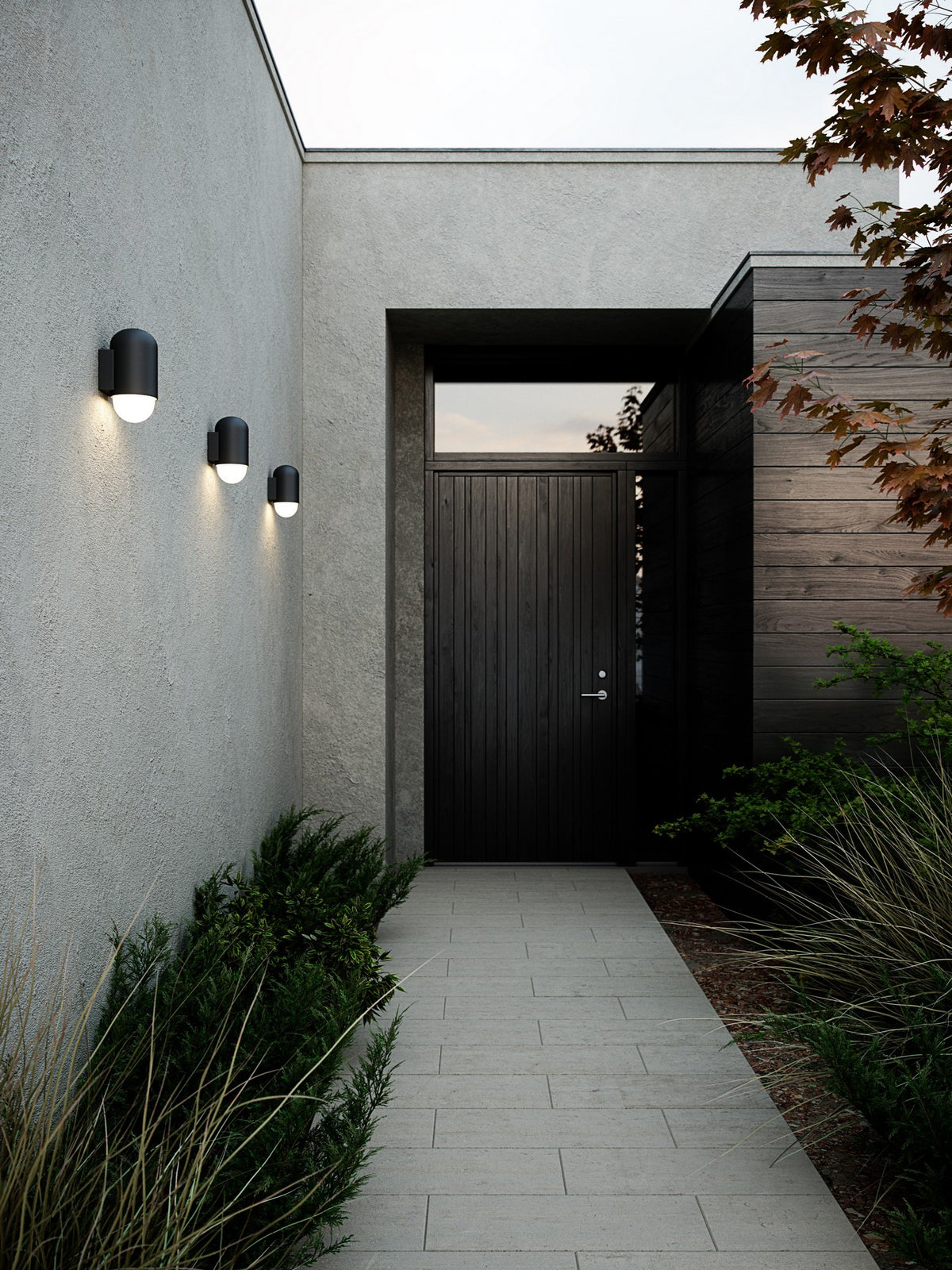 Mise en ambiance extérieure, trois appliques noires alignées sur un mur de béton gris