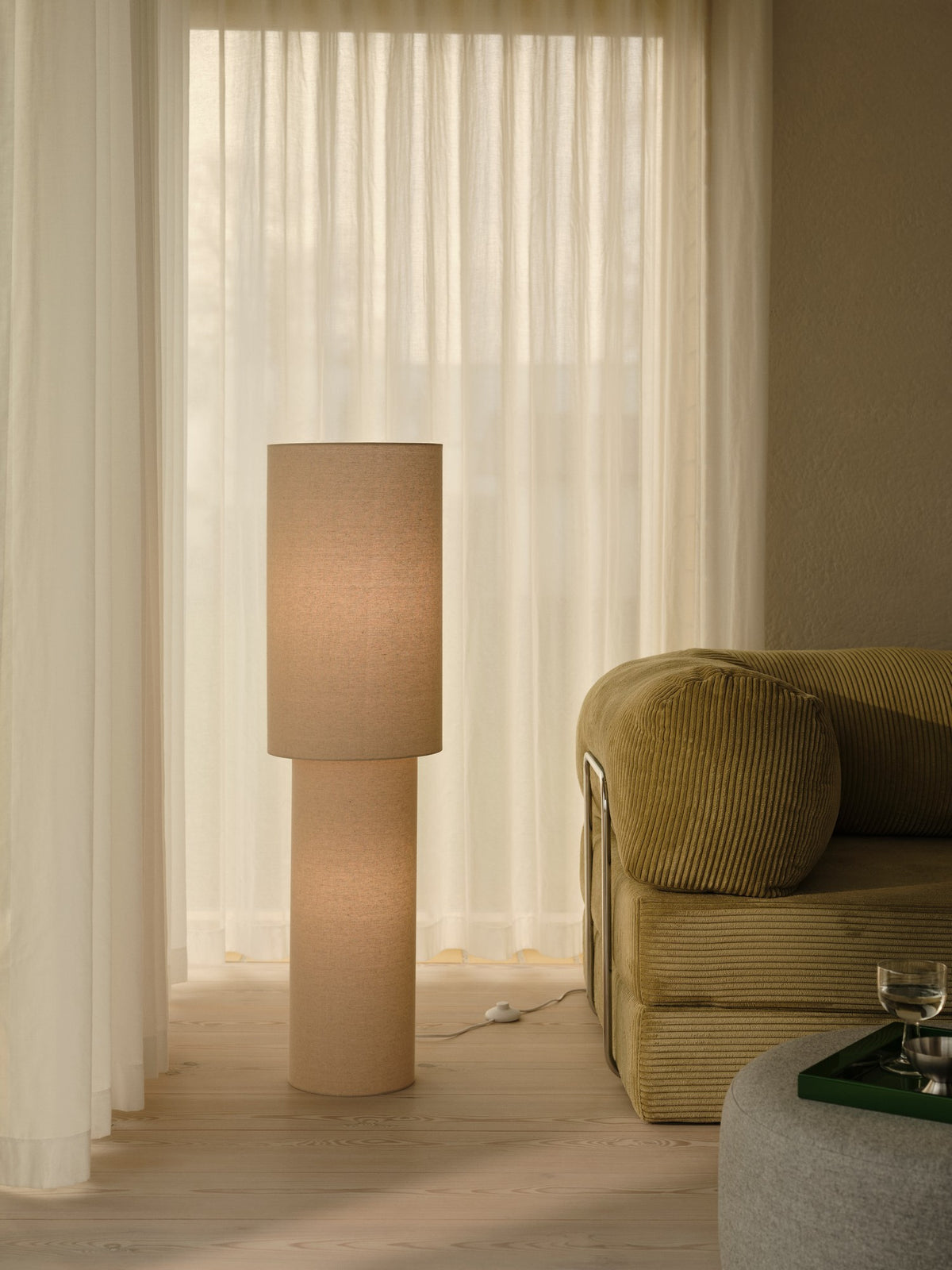 Lampadaire allumé en salon devant des rideaux, près d'un canapé vert