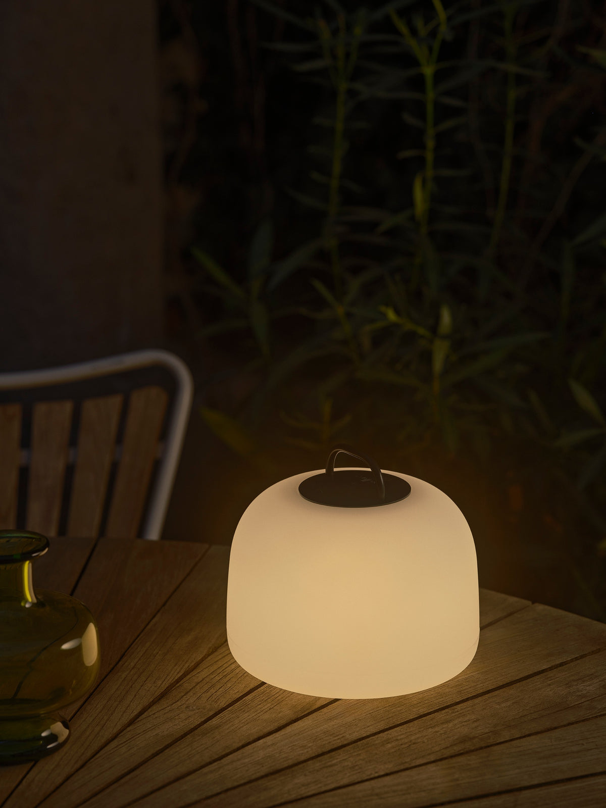Ambiance nocturne : lampe allumée posée sur une table en bois extérieure.