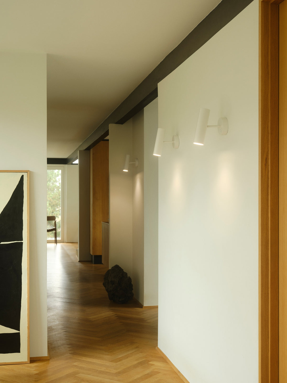 Mise en ambiance de trois appliques murales blanches dans un couloir contemporain.