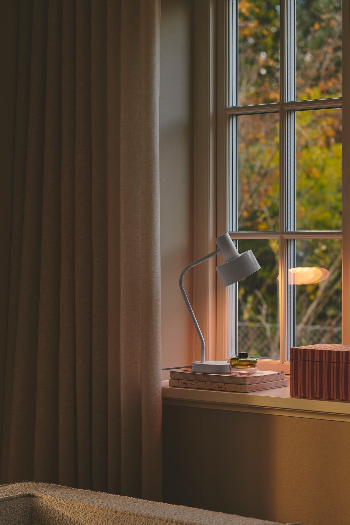 Mise en ambiance, lampe posée sur un rebord de fenêtre devant un rideau beige