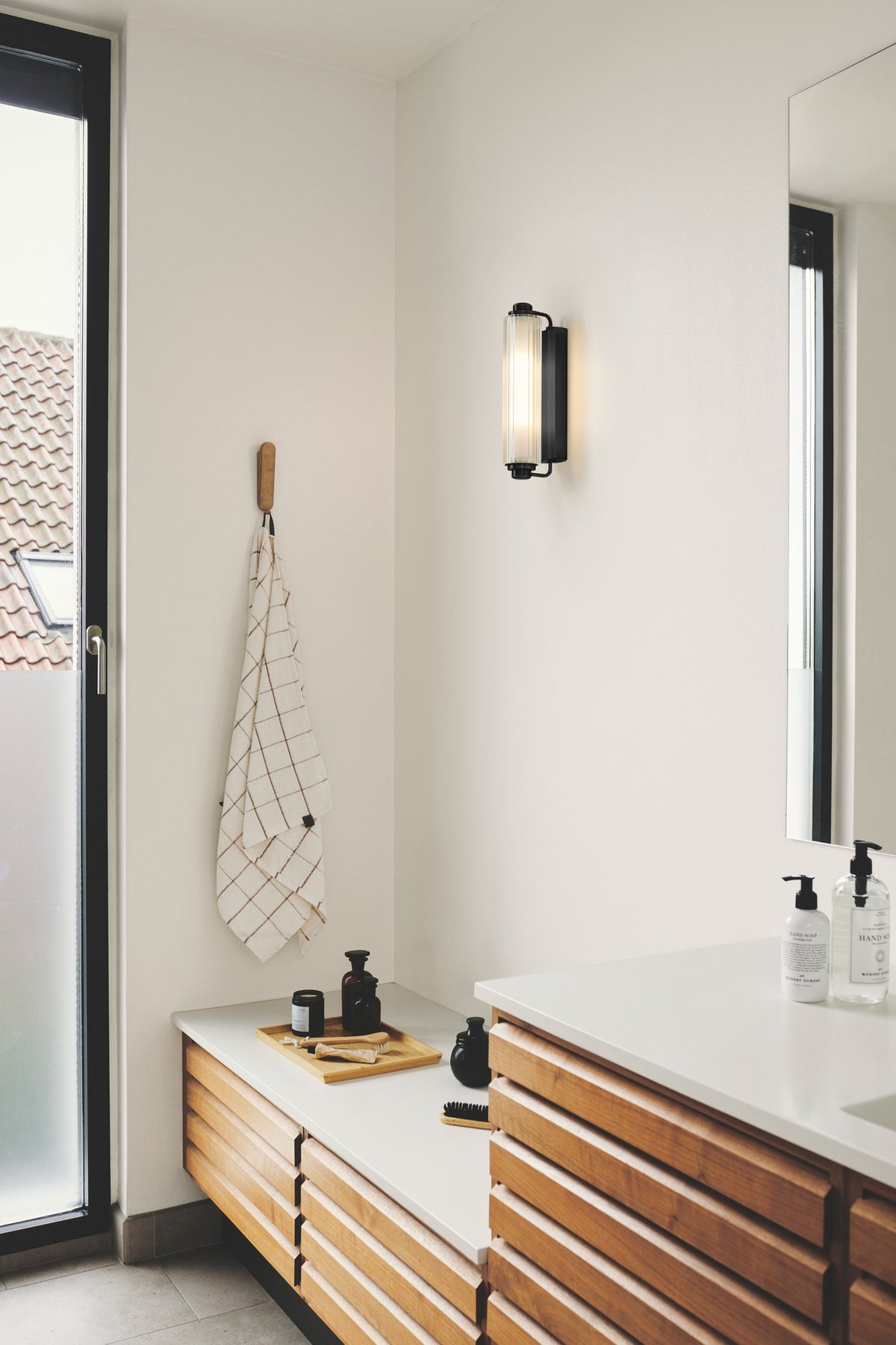 Mise en ambiance dans une salle de bain avec applique murale allumée au-dessus d'un meuble.