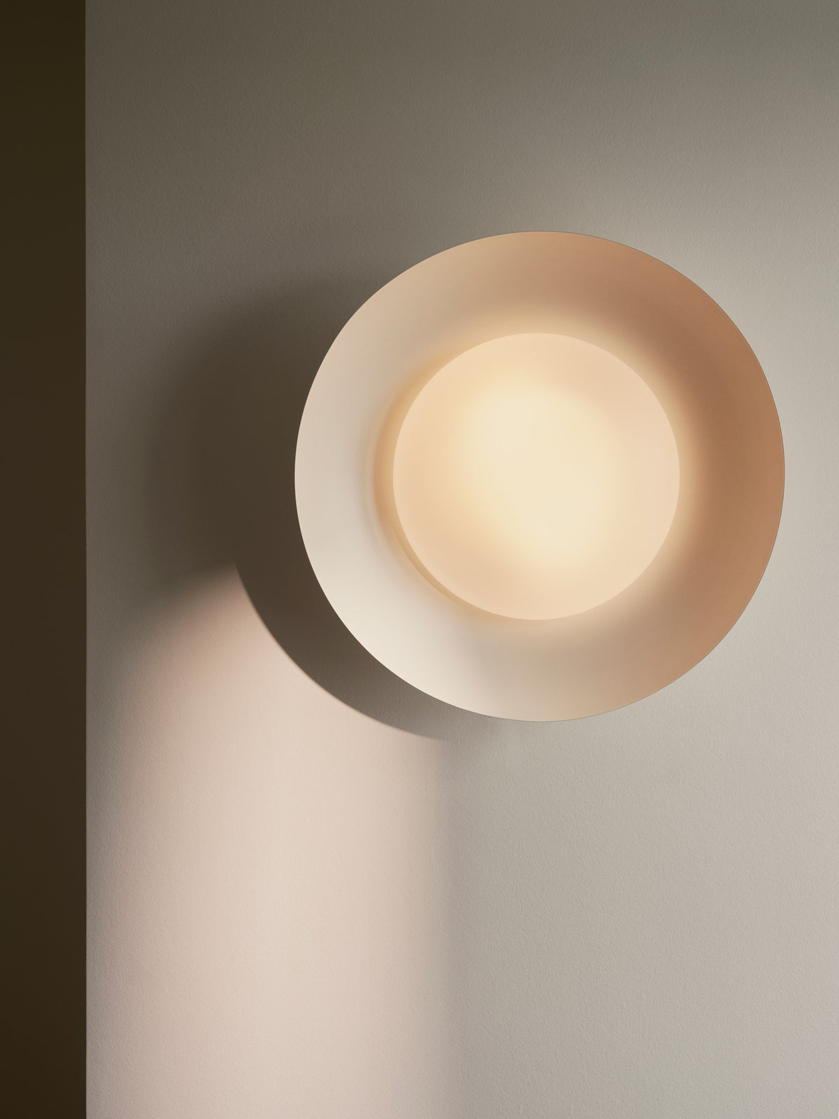 Gros plan sur le luminaire mural allumé, halo lumineux et ombre portée sur le mur.