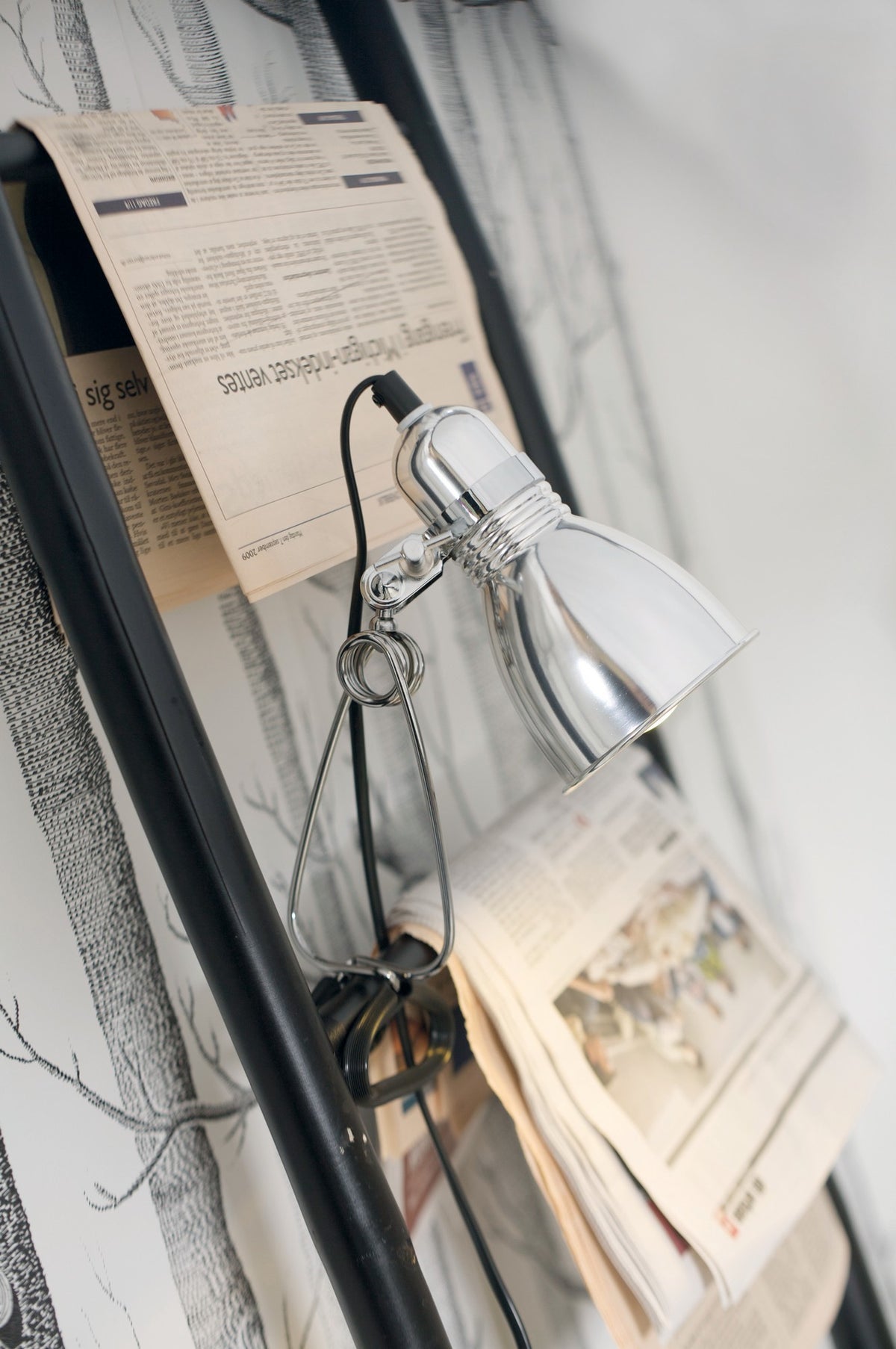 Mise en ambiance de la lampe à pince fixée sur support, près de journaux
