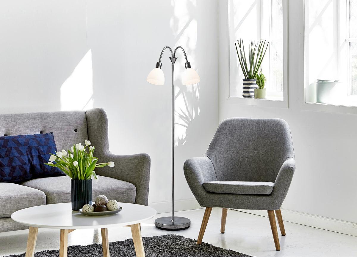 Lampadaire double allumé dans un salon contemporain, canapé gris, table basse blanche et plante.