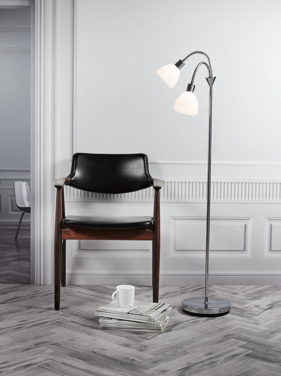 Lampadaire double éclairé près d'un fauteuil noir en cuir, sol en chevrons et magazines.