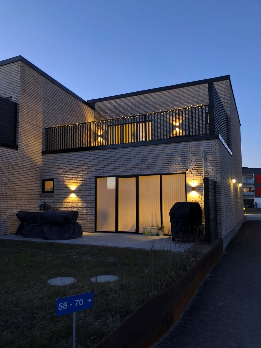 Maison en briques au crépuscule, plusieurs appliques murales éclairant la façade en haut et en bas