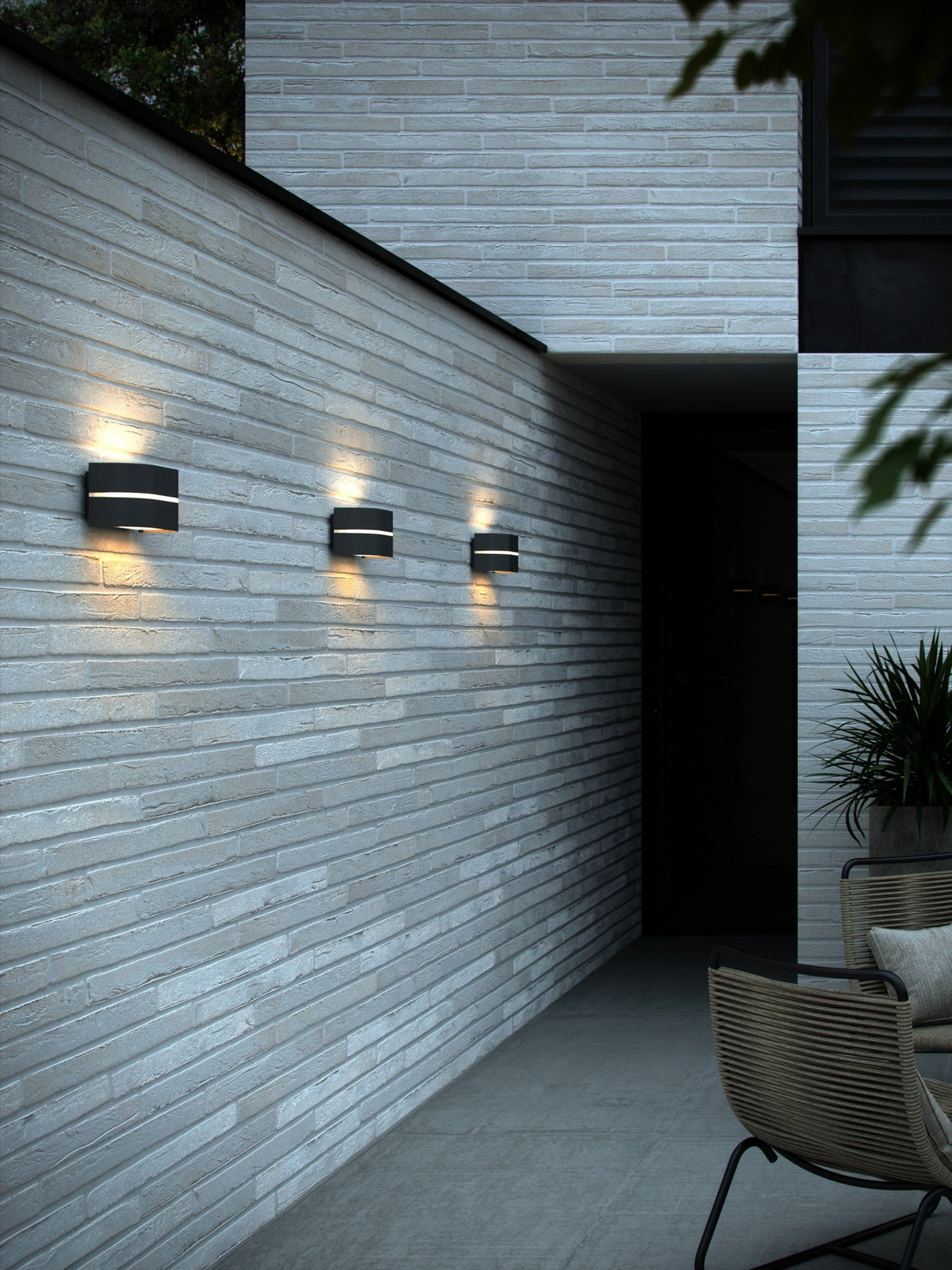 Mise en ambiance nocturne de trois appliques sur une façade en brique blanche