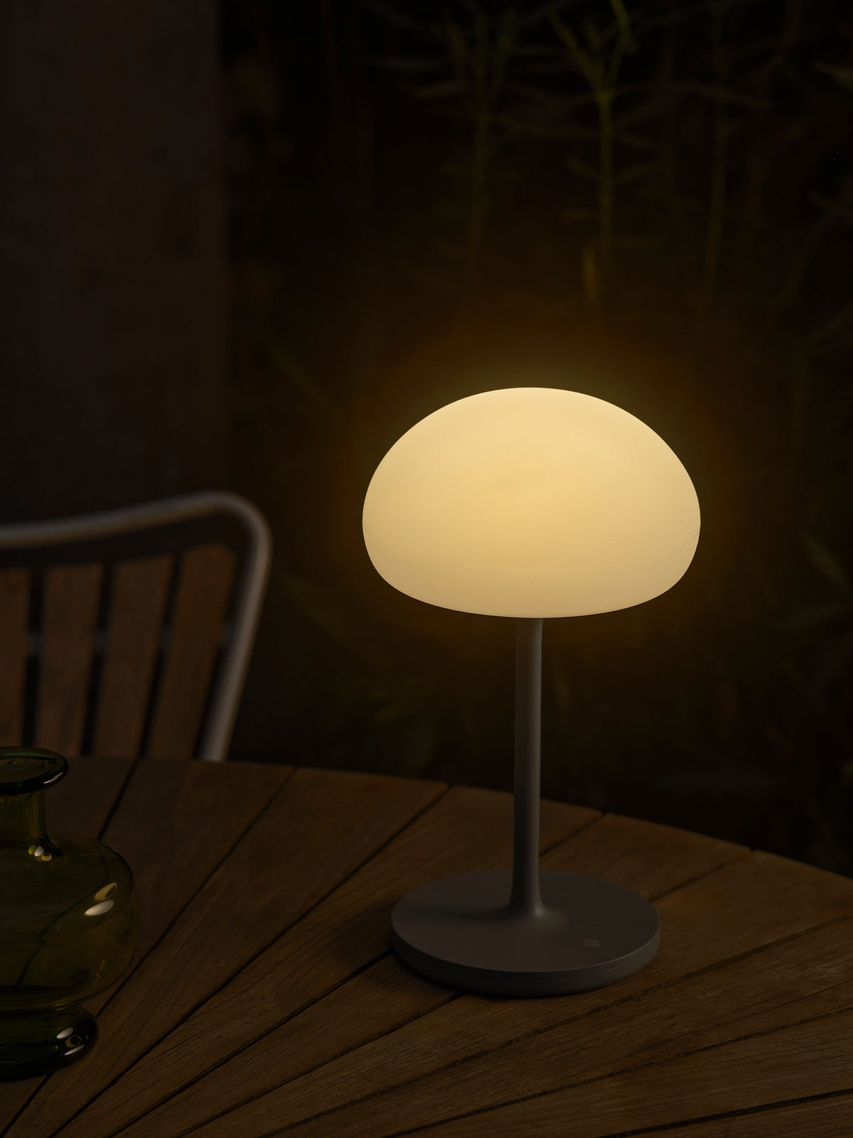 Lampe posée sur table en bois le soir, ambiance chaleureuse dans un jardin.