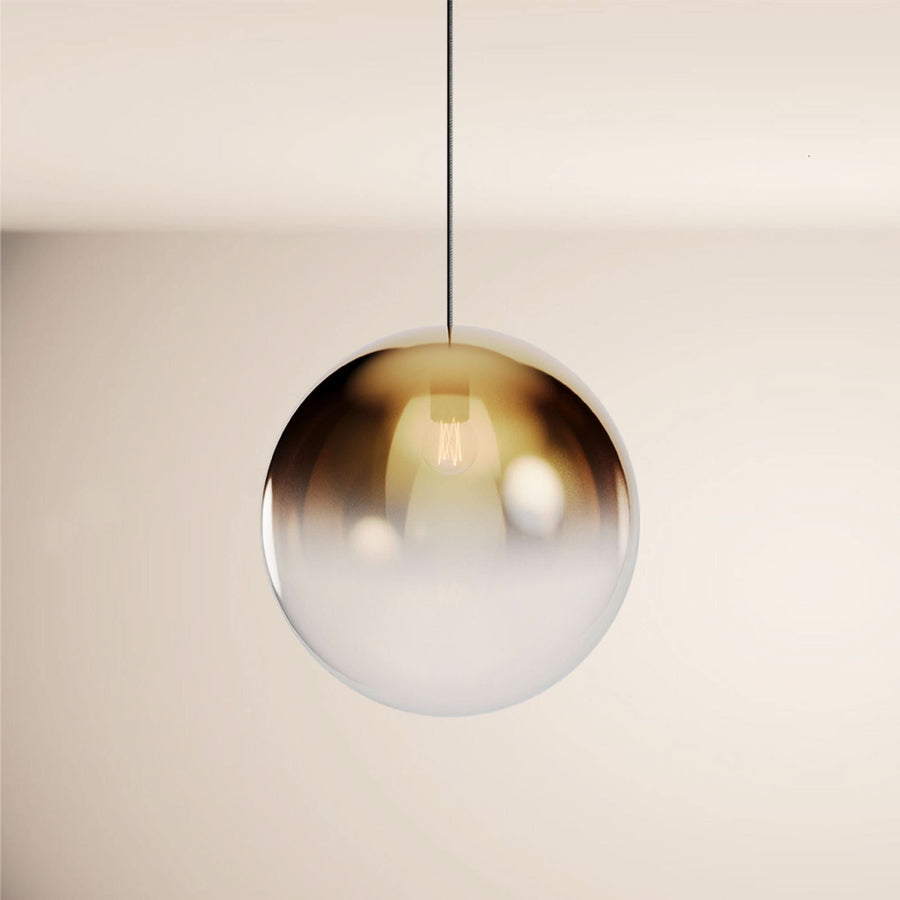Vue rapprochée d'un globe en verre dégradé ambré et blanc, suspendu par un câble noir.
