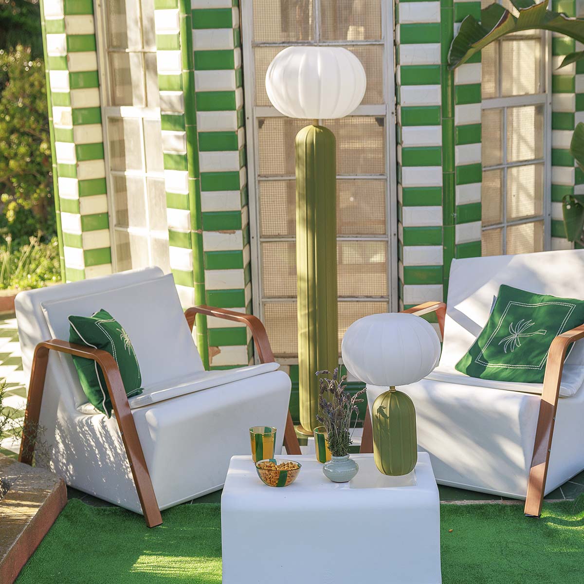 Lampadaire vert olive et sa version de table sur un patio ensoleillé, fauteuils blancs.