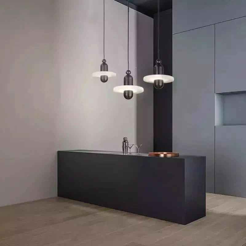 Trois suspensions noires alignées au-dessus d'un comptoir sombre, décor minimal gris.