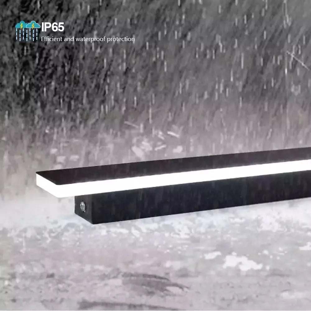 Détail produit sous une pluie battante, applique linéaire noire avec mention IP65 étanche.