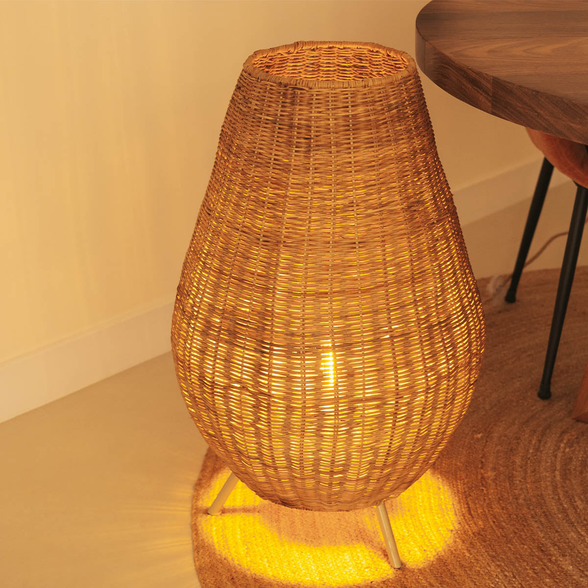 Vue de face du luminaire : abat-jour tressé et trois pieds métalliques fins