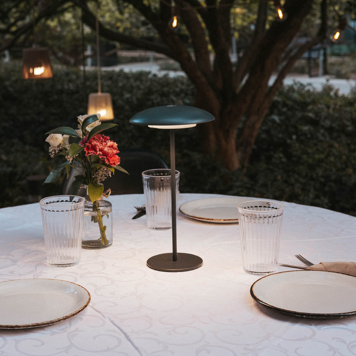 Lampe à poser bleu-vert allumée sur table dressée dans un jardin en soirée