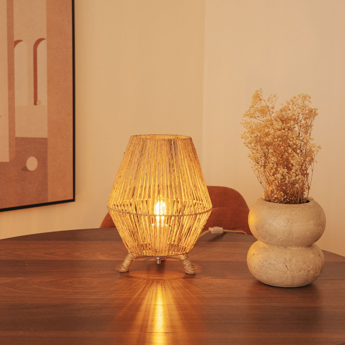 Lampe posée sur une table en bois, à côté d'un vase en béton, fleurs séchées.