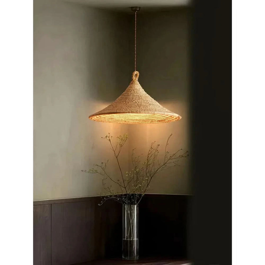 Luminaire suspendu allumé éclairant un vase transparent rempli de fines branches.