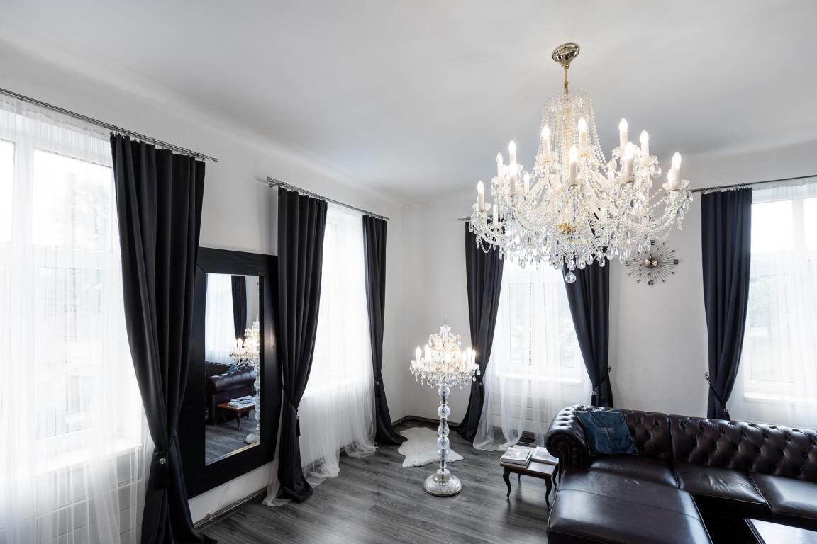 Pièce claire avec rideaux noirs, lustre au plafond et lampadaire cristal assorti près du canapé.