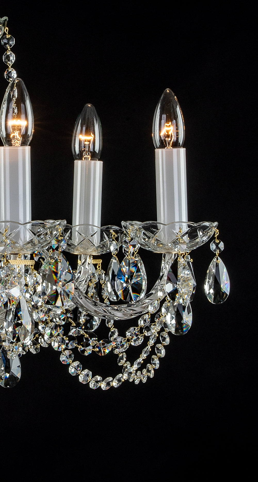 Détail de trois bras du lustre, bobèches ciselées, pendentifs en cristal et ampoules allumées.