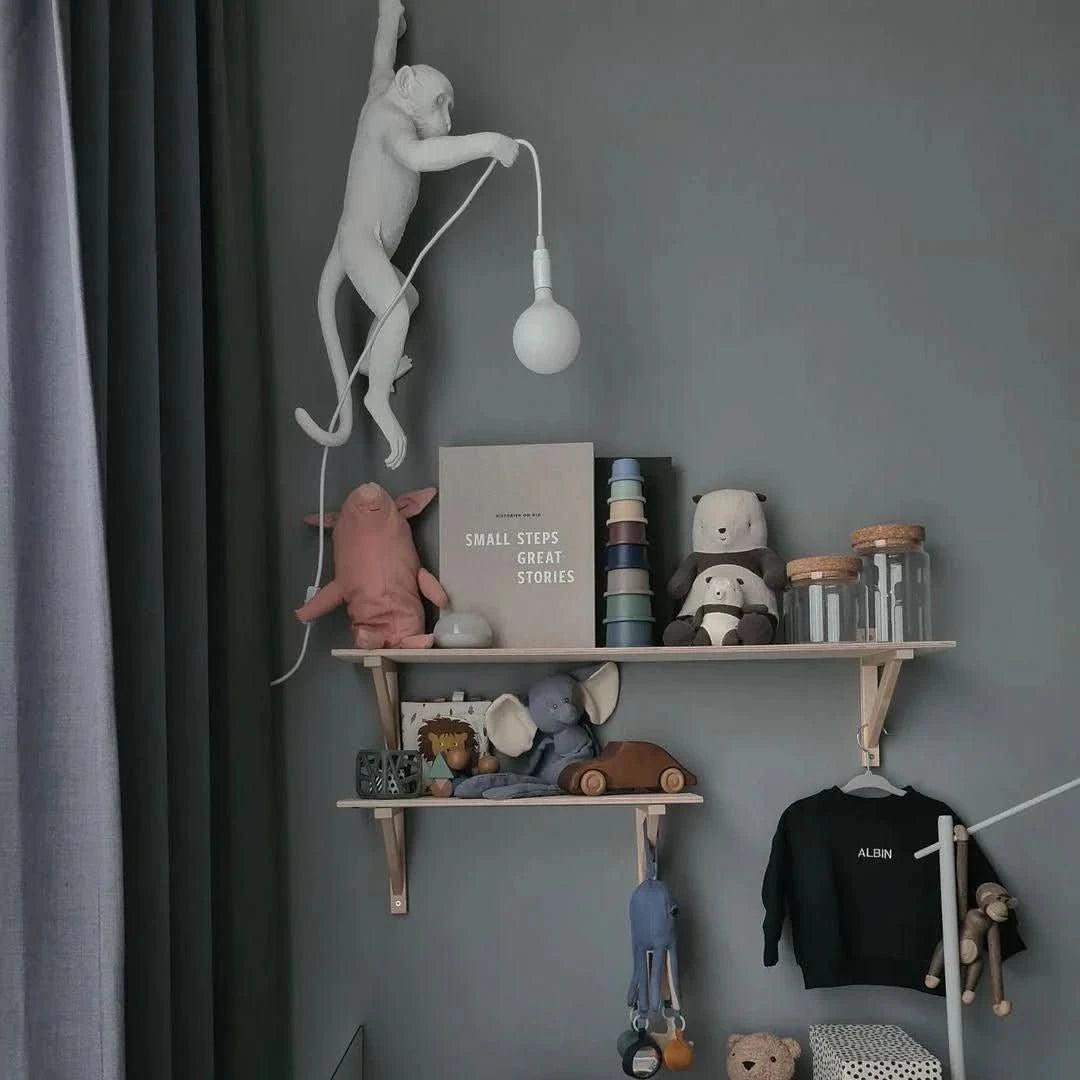 Mise en ambiance enfantine avec singe blanc accroché au mur au-dessus d'une étagère