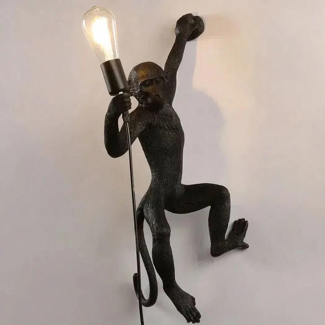 Applique murale noire en forme de singe suspendu brandissant une ampoule allumée