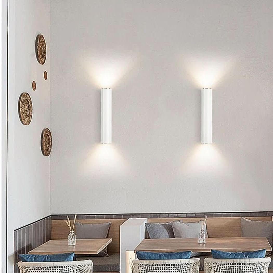 Deux appliques murales blanches éclairant un mur blanc au-dessus d'une banquette de restaurant.