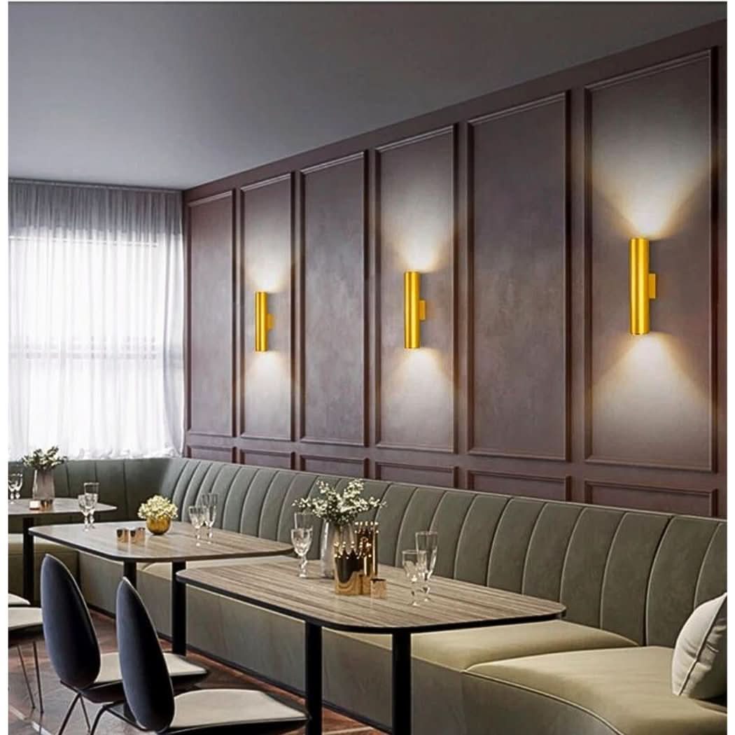 Trois appliques dorées fixées sur panneaux muraux marron foncé dans une salle de restaurant.