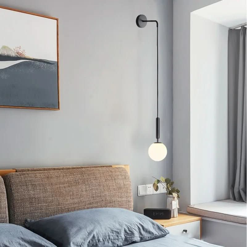 Variante noire mate de l'applique, boule opaline allumée près d'un lit aux tons bleu-gris