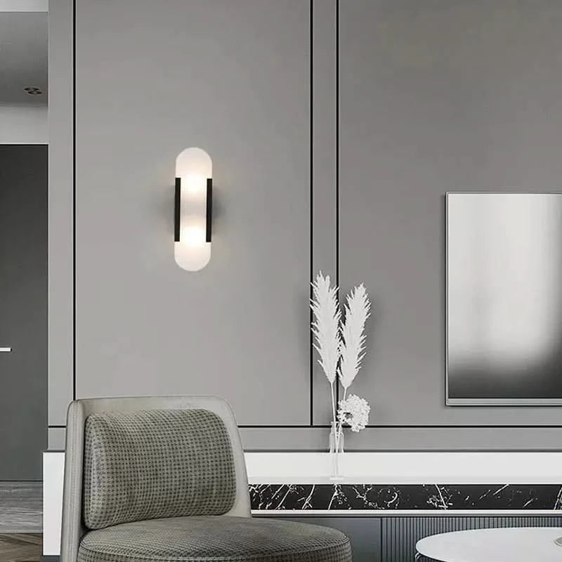 Applique noire allumée sur mur gris, fauteuil et vase de fleurs séchées