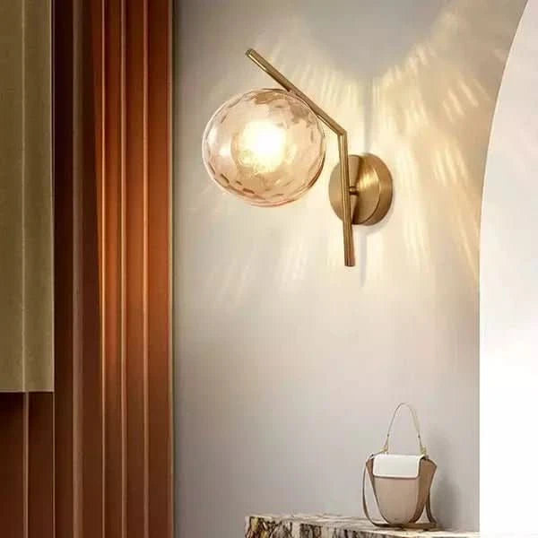 Applique murale dorée avec globe en verre ambré texturé, lumière chaude et reflets sur le mur