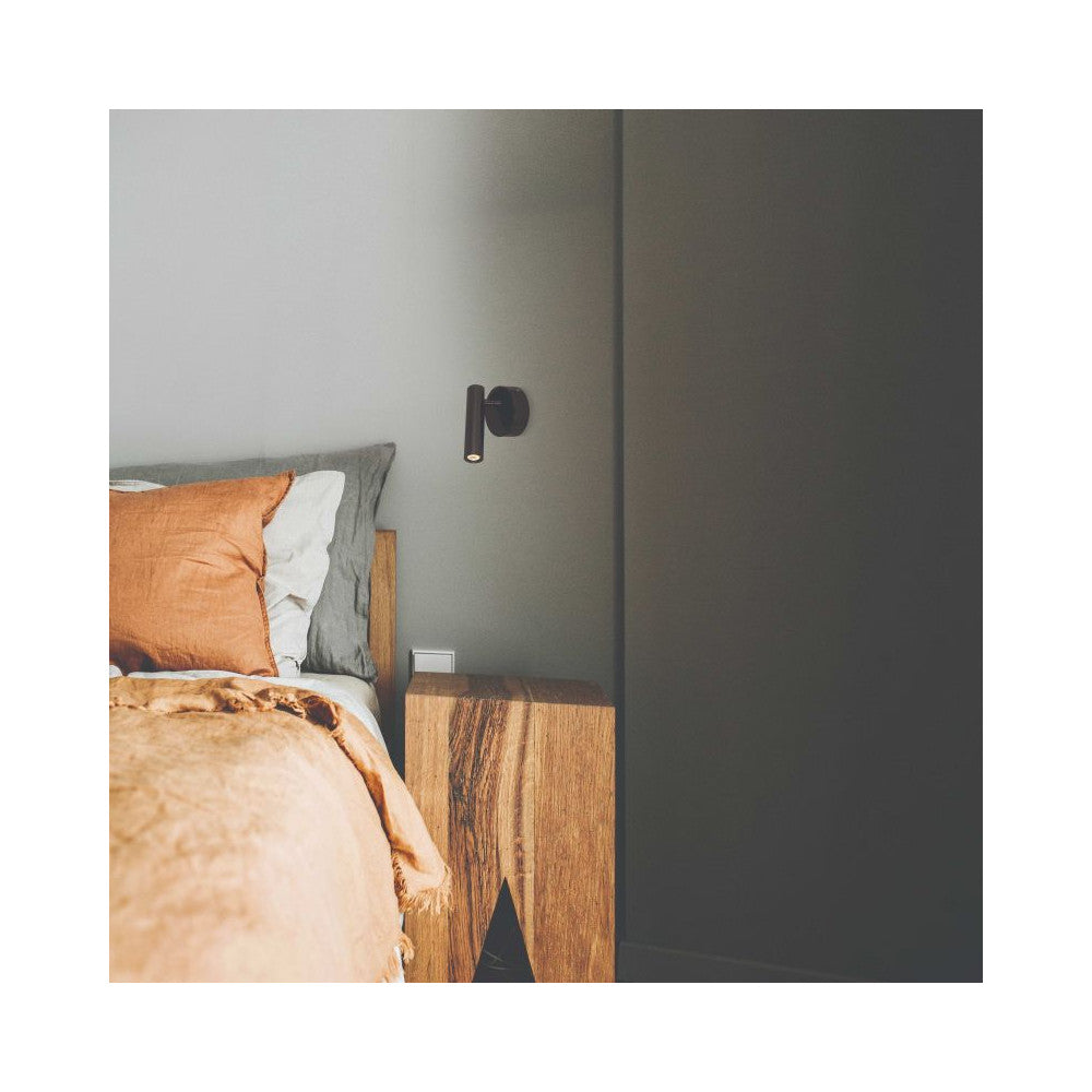 Applique noire allumée près d’un lit, ambiance chambre avec bois et textiles.