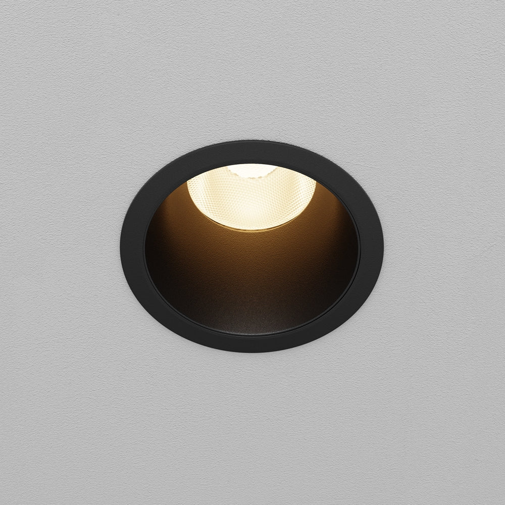 Spot encastré rond dans un plafond gris, vu de face avec halo lumineux