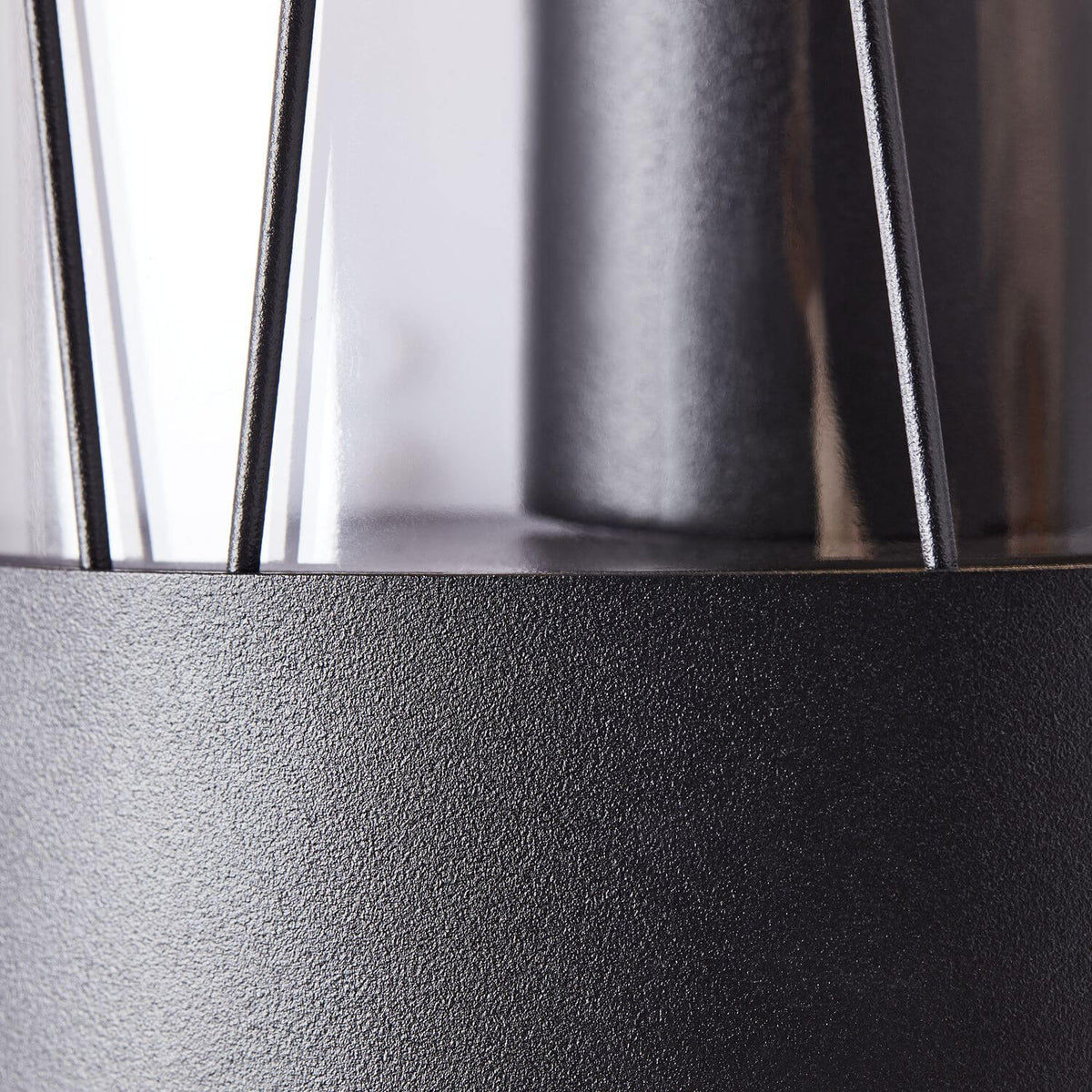 Gros plan sur la finition noire martelée et les tiges verticales du luminaire.