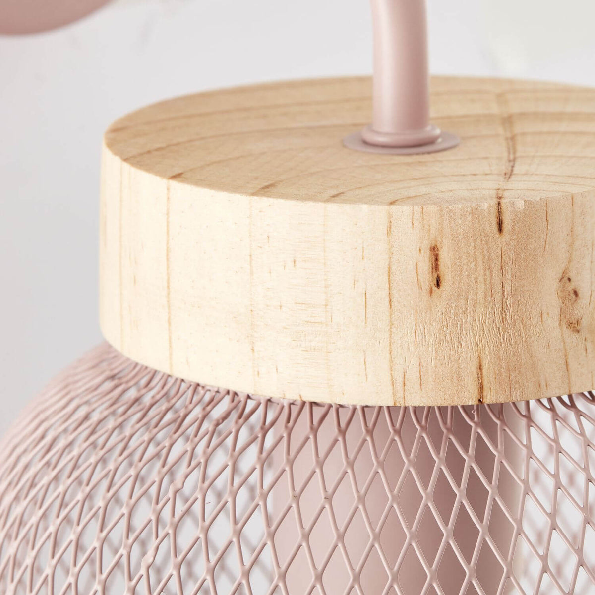 Gros plan sur la finition, cylindre de bois brut et maille métallique rose tressée.