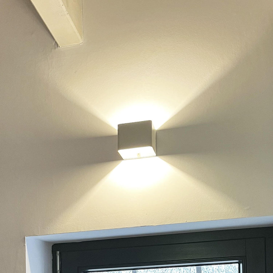 Luminaire mural blanc installé près d'une porte, lumière chaude diffusée vers le haut et le bas.