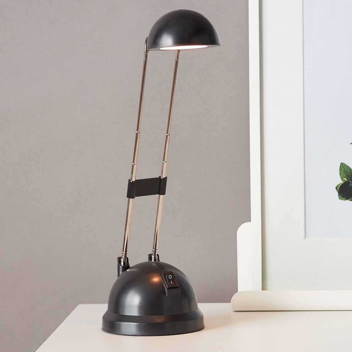 Lampe allumée posée sur un bureau, près d'un cadre blanc, ambiance intérieure chaleureuse