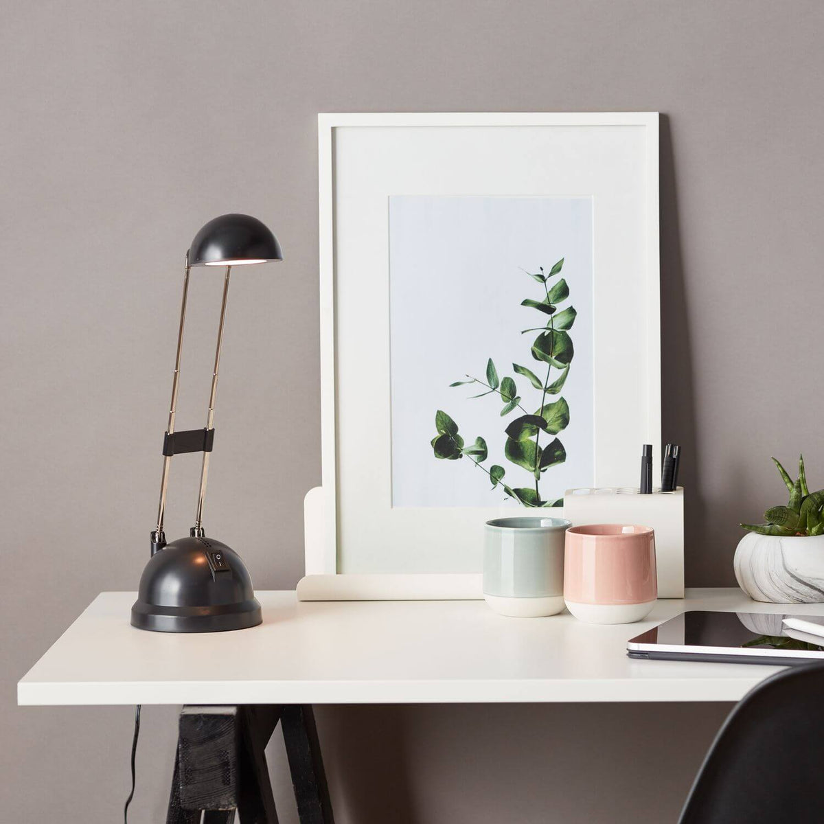 Mise en ambiance du bureau blanc, lampe noire près d'un cadre végétal et de tasses colorées