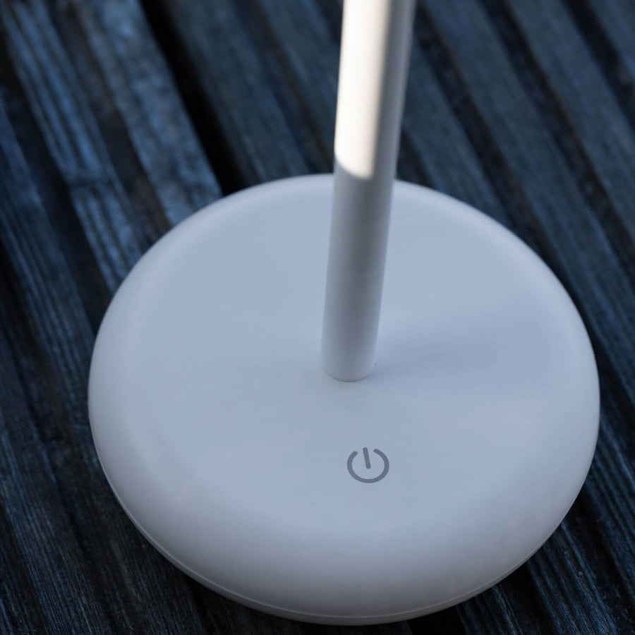 Détail du socle blanc avec bouton tactile intégré, posé sur une table sombre